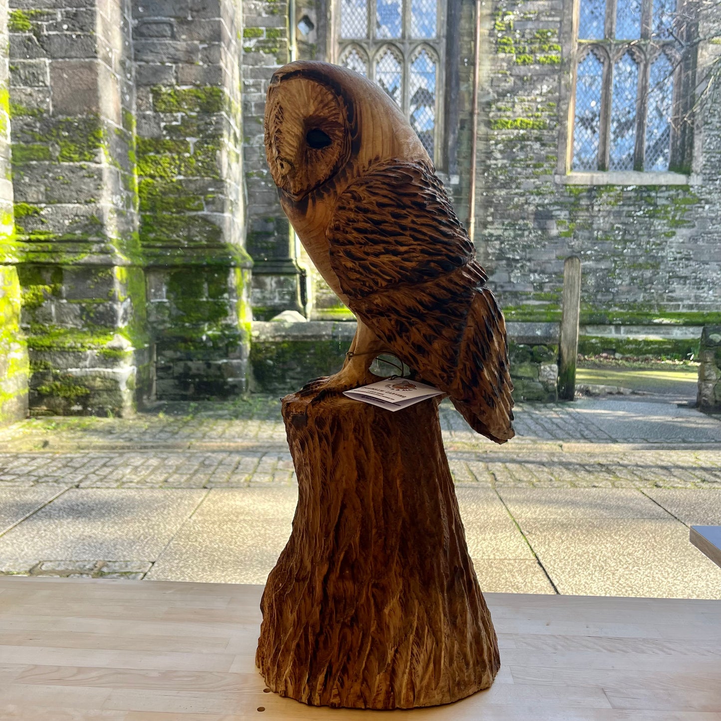 Wooden owl sculpture on a tree stump in front of a stone building with large windows.