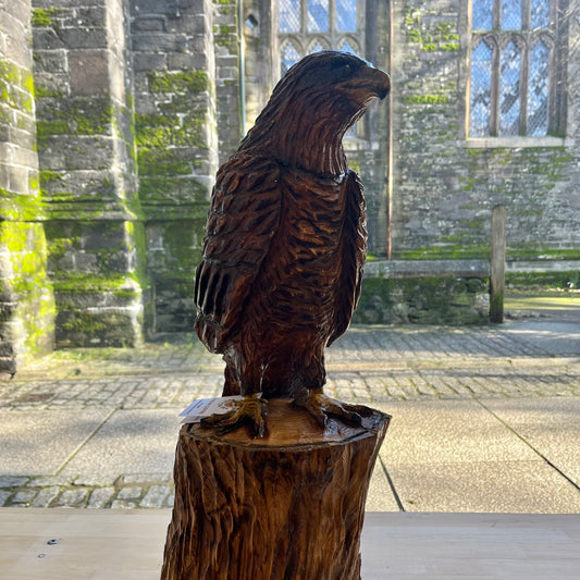 Wooden sculpture of an eagle on a tree stump in front of stone building.