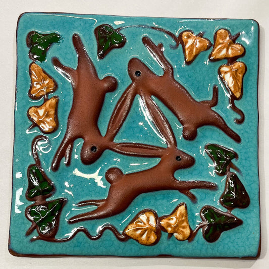 Ceramic tile with brown rabbits and green leaves on a blue background