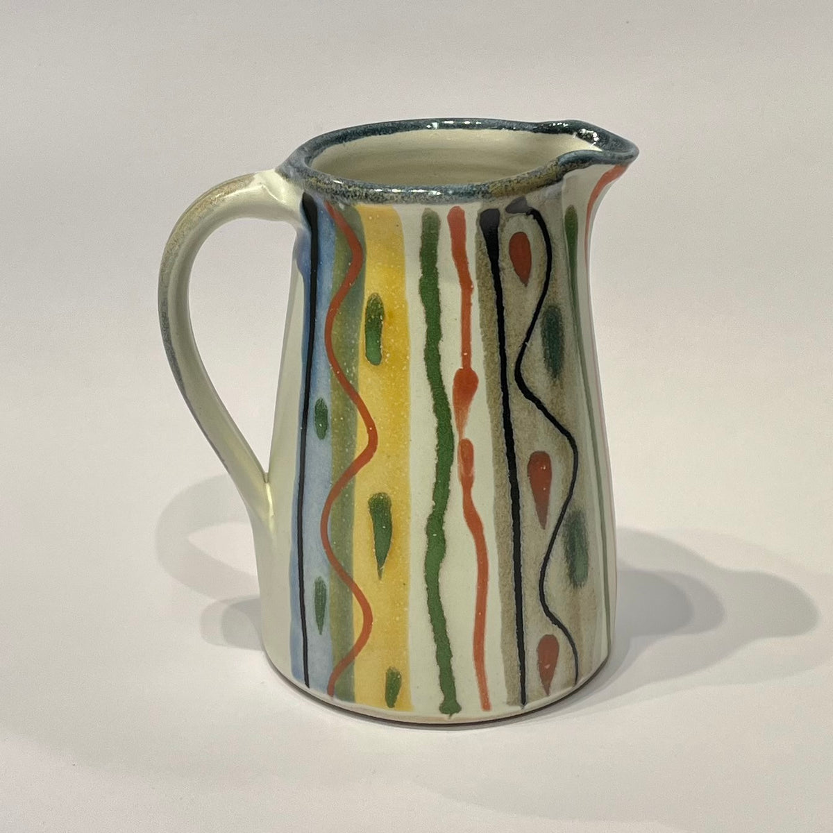 A ceramic Jug  decorated with abstract vertical wavy lines and dots in black, green, orange, and yellow