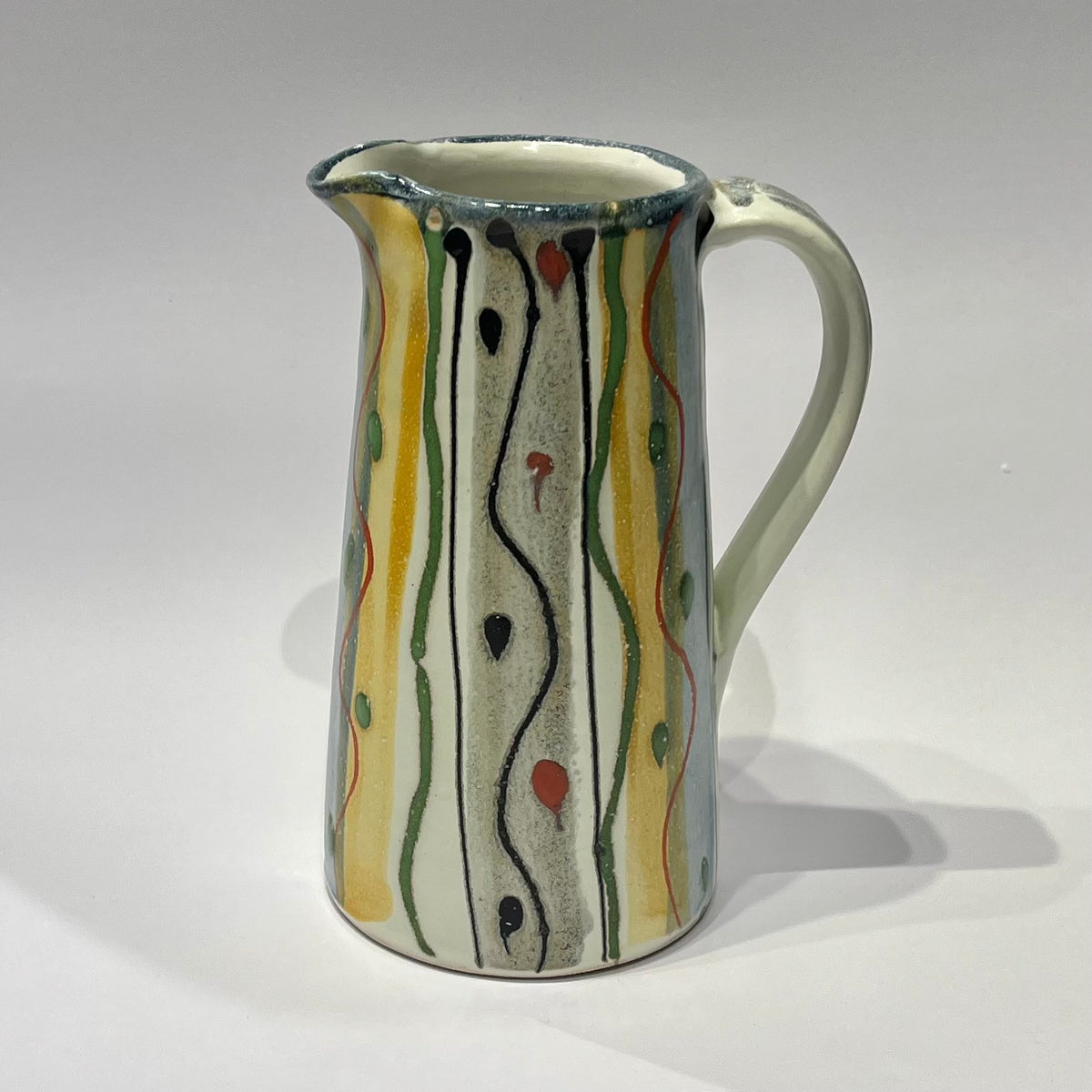A large ceramic Jug  decorated with abstract vertical wavy lines and dots in black, green, orange, and yellow