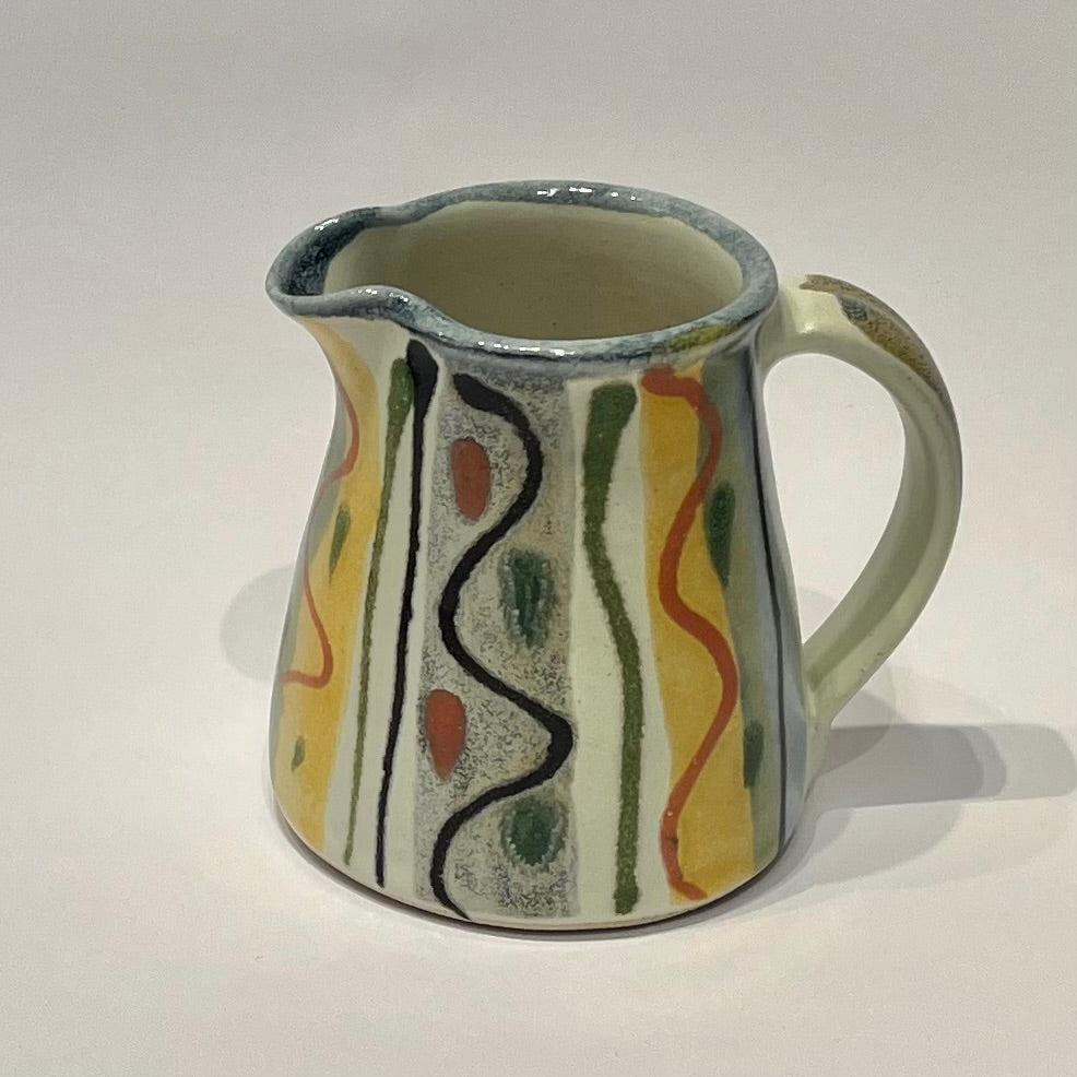 A ceramic Jug  decorated with abstract vertical wavy lines and dots in black, green, orange, and yellow